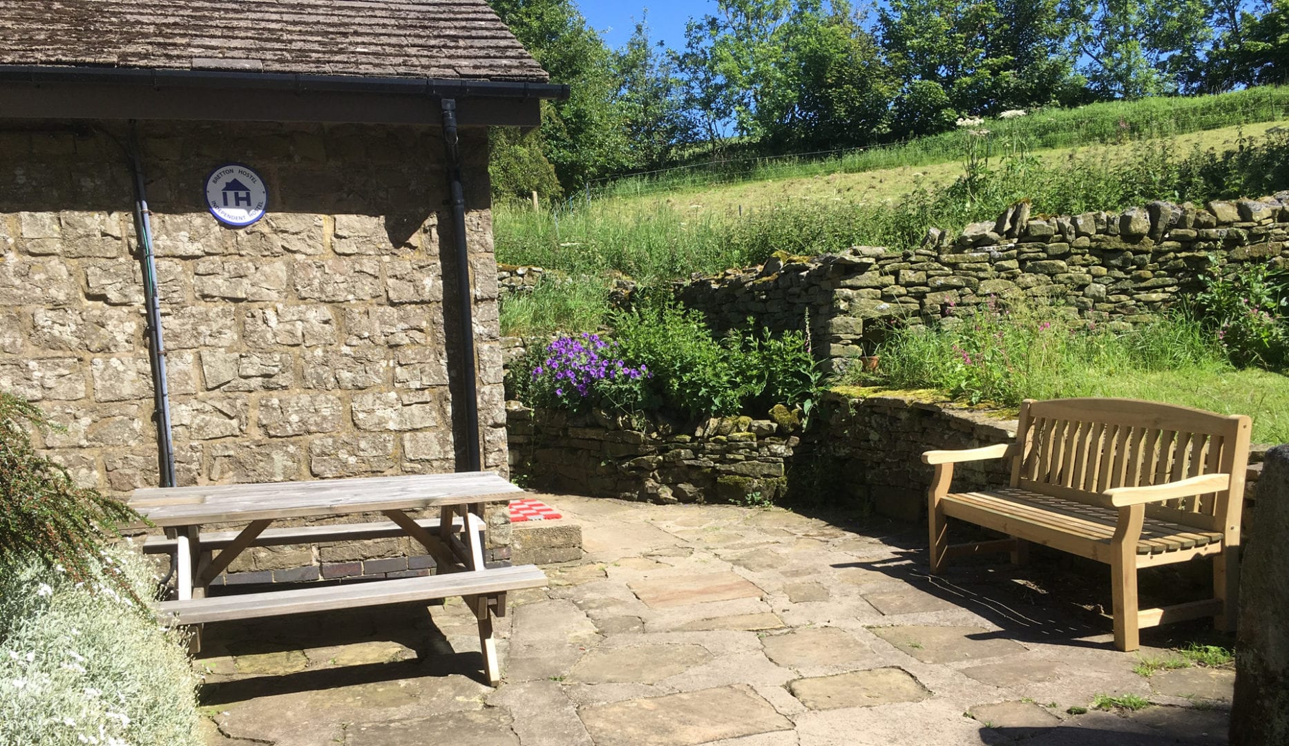 Bretton Independent Hostel exterior with Indepdent Hostels logo on the wall. There are also picnic tables nearby.