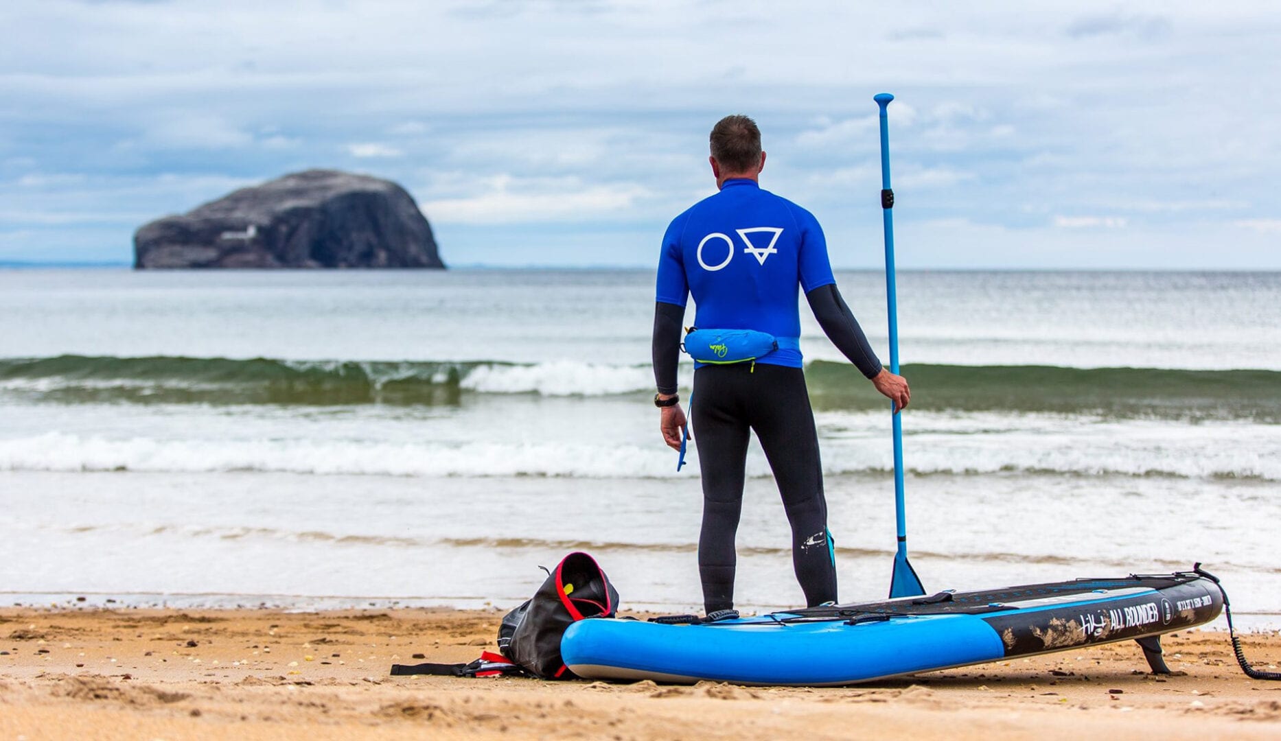 lone paddle boarder on the beach with his paddle, his board adn his dog