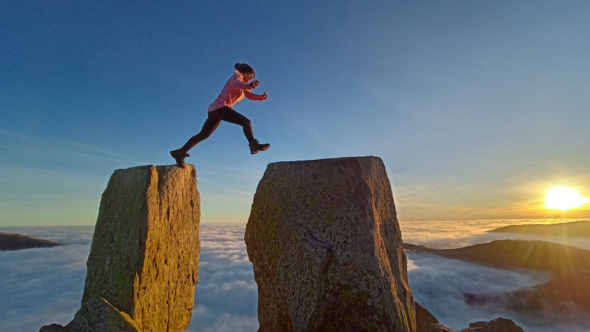 person jumping between two rock stacks in the mountains with the clouds belpw