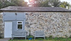 Front exterior view of the stone bunkhouse with grey wooden benches