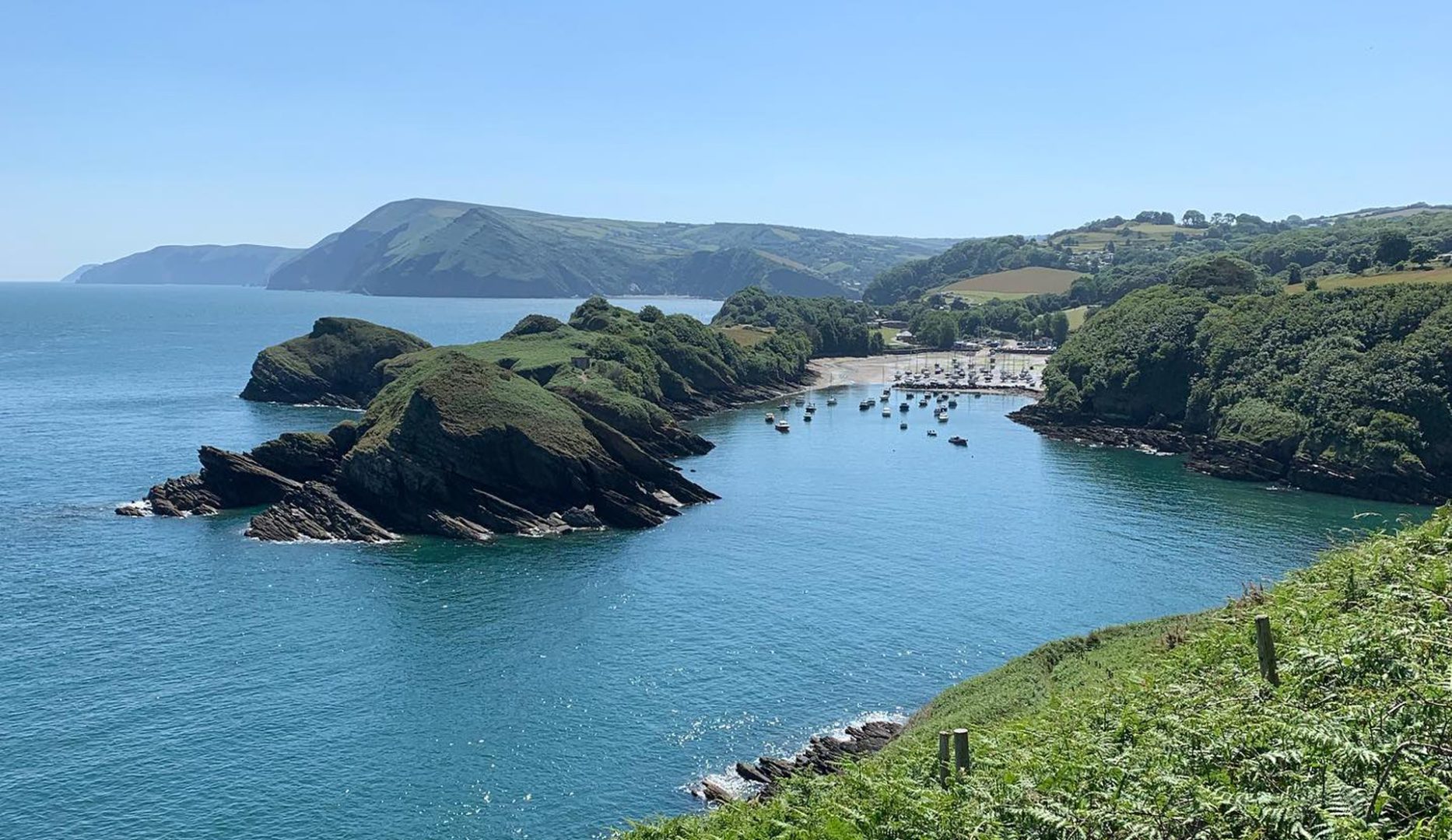 north devon coast showing cliff paths and boats in a distant harbour