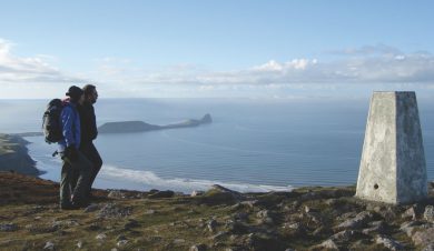2 walkers by a trig point overlooking Rhossili bay
