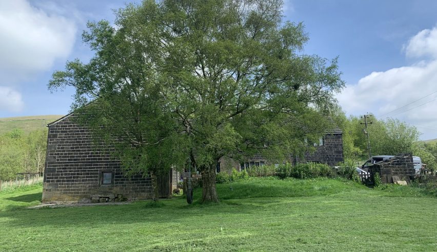 EXterior of stone hostel with large leafy tree and lawn
