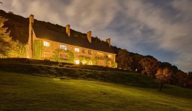 Front view of stone hall with lights in rooms, lit by the evening sun