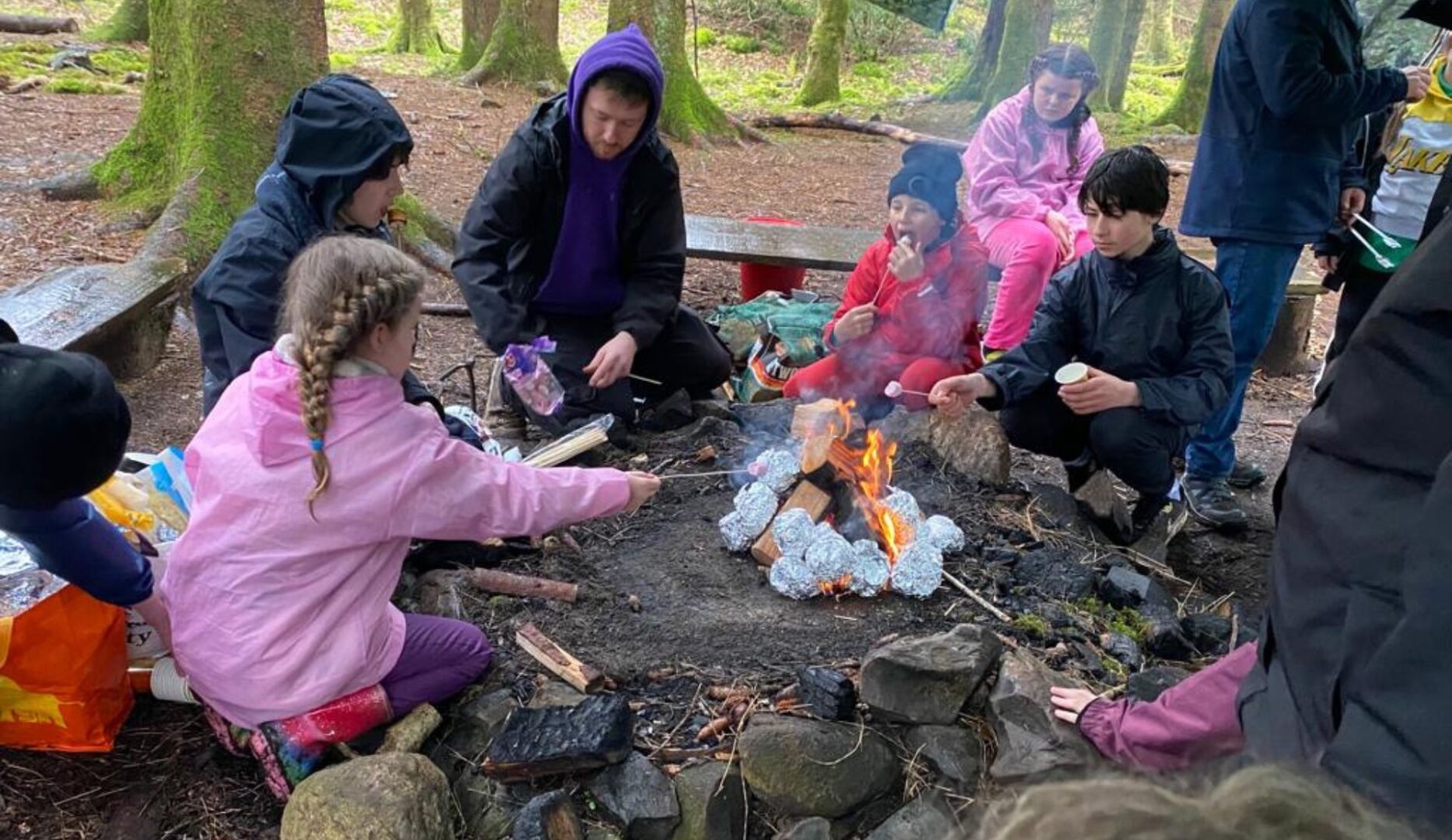 Children adn adults around a campfire baking potatoes