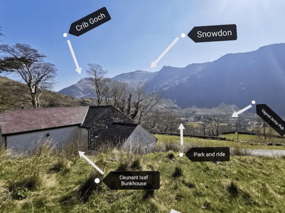 View of the stone Ceunant Isaf BUnkhouse, with arrows to Crib Goch, Snowdon, the local pub and the park and ride.