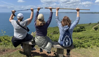 3 ladies sittig on a bench overlooking the cornish coast on a beautiful sunny day