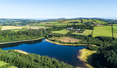 View over Wistlandpound Reservoir showing feilds and hills and Calvert Lodges in the foreground