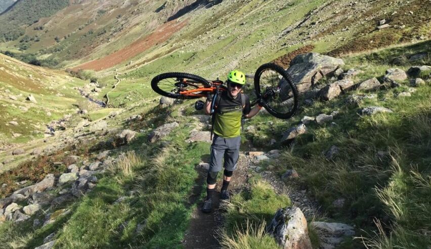 cyclist holding mountatin bike on his sholders on the fells above Witherslack Cycle Barn