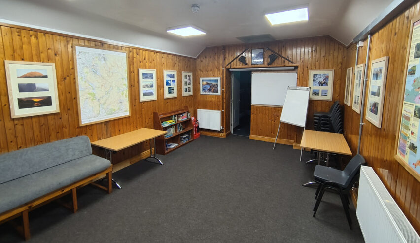 wood pannled lounge at yr hafod scout hostel showig maps on the wall tables and seating