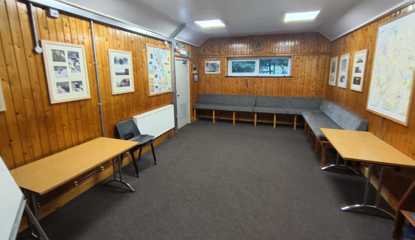 wood pannled lounge at yr hafod scout hostel showig maps on the wall tables and seating