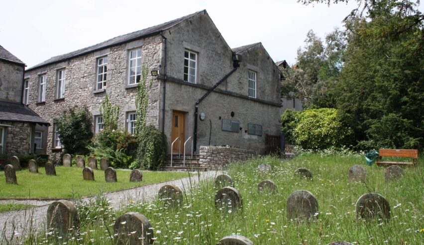 view of Yealand Old School accommodation accross the quaker church graveyard with daisys in the grass