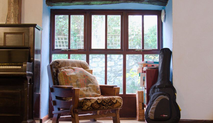 armchair in front of a large windpw with piono and guitar