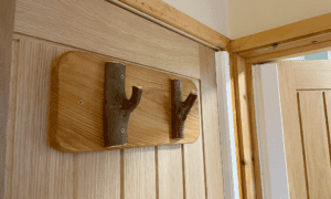 Two coat hooks on the back of a door, made from tree branches left with natural bark on.