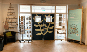 Interior of a gift shop with double doors pained with vines, card stands and trinkets displayed around the sides of the room
