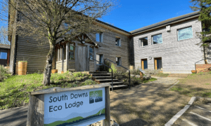 Two storey wooden building with steps up to an entrance porch, and sign reading 'South Downs Eco Lodge'