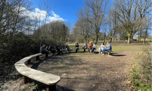 10 people sat on a horseshoe shaped bench, eating melas from the cafe.