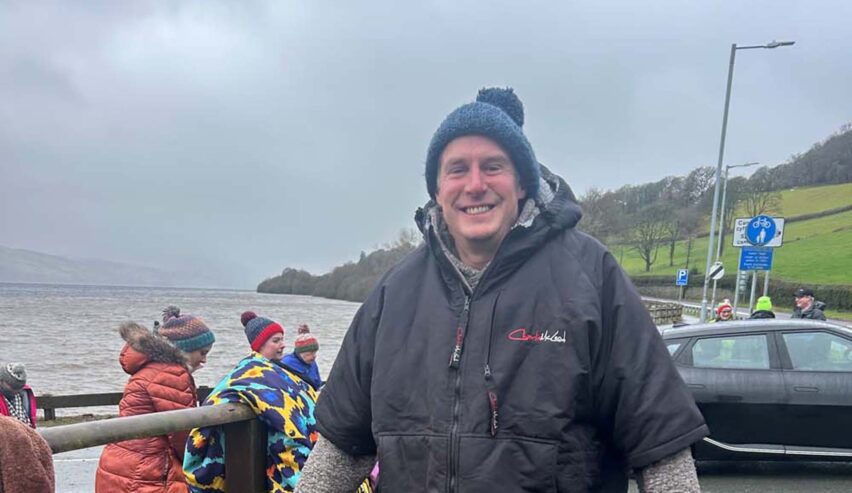 man in bobble hat and warm suit after wild siming in the sea